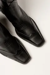 Bota de cuero negra con caña media, punta fina y taco bloque. Diseño estilo western con bordados decorativos.