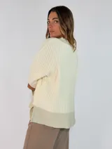 Sweater de tejido acanalado en color marrón oscuro, con cuello en V y detalles en tono metalizado en el cuello, puños y ruedo. Presenta un corte holgado y mangas largas.