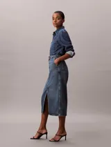 Falda midi de denim azul de talle alto, con diseño carpenter, cierre frontal de botón y cremallera, bolsillos y abertura central delantera.
