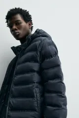 Campera puffer acolchada de corte regular fit en color negro, confeccionada en tejido técnico repelente al agua. Presenta cuello subido con capucha, cierre frontal de cremallera, mangas largas con puños elásticos y bolsillos laterales de vivo.