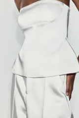 Top palabra de honor de tejido satinado blanco, con escote recto y diseño con bajo tipo peplum y costuras marcadas.