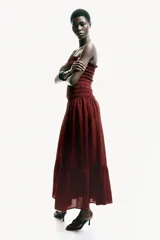 Vestido midi strapless de color bordó, con cuerpo fruncido elástico y falda larga acampanada con un volante en el bajo.