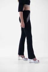Pantalón negro de corte flare, tiro alto, con detalles de flecos de strass en los bolsillos laterales.