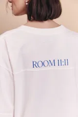 Remerón de corte oversize color off-white, con cuello redondo y mangas cortas. Presenta estampados en color azul que incluyen un dibujo de un edificio, una llave con forma de corazón y la palabra 'renée'.