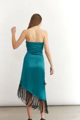 Vestido midi sin mangas color turquesa, con escote strapless y detalle de nudo frontal. El ruedo presenta un corte asimétrico con flecos negros largos.