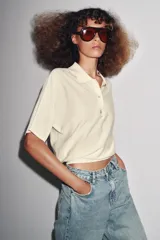 Polo de punto color crema, de manga corta y corte holgado, con cuello polo y tres botones frontales.