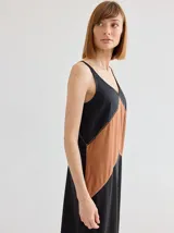 Vestido midi de corte recto y escote en V, con diseño bicolor que combina paneles en negro y tostado en forma de V invertida. Presenta costuras decorativas visibles en la unión de los colores.