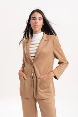 Blazer de gamuza con solapas clásicas, cierre frontal de doble botón y bolsillos laterales. Presenta un corte estructurado con hombreras.