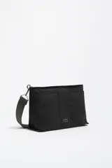 Bolso bandolera de tamaño mediano confeccionado en nylon negro, con estructura blanda, asa regulable de tejido, logo metálico de la marca en el frente y cierre con cremallera.