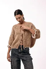 Saco de tejido de punto color beige con frente abierto y cierre mediante lazos frontales. Presenta mangas amplias con terminaciones en volados con borde en contraste blanco.