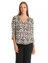 Blusa de seda fría con estampado geométrico tipo ikat en tonos beige y negro. Presenta escote en V, botones decorativos en la parte frontal y mangas tres cuartos con detalle de tajo en los puños.