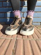 Zapatillas deportivas de cuero color peltre, con cordones negros y suela de goma blanca.