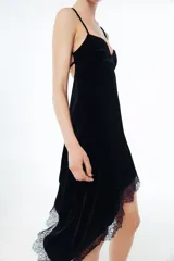 Vestido midi de terciopelo negro con escote en pico y tirantes finos ajustables. Presenta un diseño asimétrico en el bajo con aplicación de encaje a tono y espalda con tiras cruzadas.
