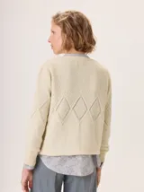 Buzo de lana color crema, tejido con textura de punto arroz en la parte superior y un patrón de rombos calados en la espalda y mangas. Tiene cuello redondo y puños acanalados.