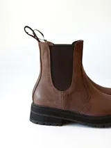 Bota tipo Chelsea de cuero color chocolate, con paneles elásticos laterales, tirador trasero y suela track negra de goma.
