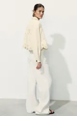 Cazadora color rosa pálido, de cuello solapa y manga larga. Tiene bordados perforados a tono en el ruedo y cierre frontal con botones color madera.