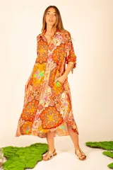 Vestido camisero midi color naranja con estampado floral y paisley. Tiene cuello camisero, mangas largas con puños abotonados, bolsillos laterales y aberturas laterales en el ruedo.
