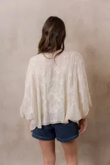 Kimono marfil de silueta amplia, confeccionado en tela con bordados florales y detalles calados. Cuenta con mangas amplias tres cuartos, frente abierto y terminaciones decorativas.