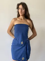 Conjunto compuesto por un pareo corto de color azul con detalle de bordado dorado en el frente y una bandana a juego. El pareo cuenta con un diseño envolvente con lazo lateral.