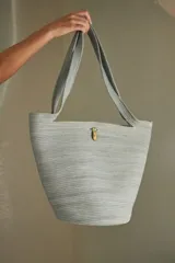 Bolso tipo tote confeccionado en soga de algodón color gris claro, con asas de hombro y cierre con broche de bronce.