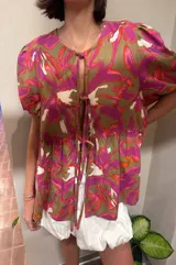 Blusa de lino bordado con estampado floral en tonos fucsia, marrón y blanco, de calce holgado, escote en V con cordones para atar y mangas cortas abullonadas.