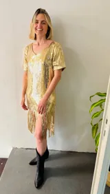 Vestido corto dorado de lentejuelas con escote en V, mangas cortas y flecos en el ruedo.