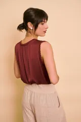 Blusa de satén color bordó, sin mangas, con cuello redondo y detalles de ribete bordado en contraste en las sisas.