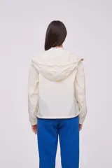 Campera liviana color crema con capucha, cierre frontal completo y cordones ajustables en el cuello y el ruedo. Cuenta con mangas largas con puños elásticos y bolsillos laterales.