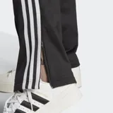 Pantalón deportivo Adidas Adicolor Classics Firebird negro con las tres tiras blancas a lo largo de las piernas, bolsillos con cierre, cintura elástica con cordón ajustable y logo bordado.