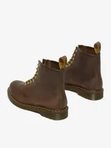 Bota Dr. Martens modelo 1460 de cuero marrón con aspecto desgastado y envejecido. Diseño de 8 ojales, con costuras amarillas, suela con amortiguación de aire resistente al aceite y lengüeta en el talón.