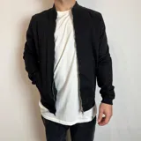 Chaqueta bomber negra de gabardina con cierre frontal, cuello redondo y bolsillos laterales.