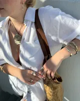 Collar artesanal con dije central de metal con textura orgánica irregular que evoca una ostra. El dije está montado sobre un cordón de algodón natural, permitiendo un uso versátil y regulable.