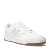 Championes urbanos New Balance de diseño minimalista, color blanco con detalles en tono crema. Presentan el logo N característico en el lateral, suela blanca con base de goma color caramelo y cierre mediante cordones.