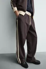 Pantalón jogger de corte wide fit en tejido compacto color gris oscuro. Presenta cintura elástica con cordón ajustable, bandas laterales en contraste color beige y costuras frontales tipo pinza.