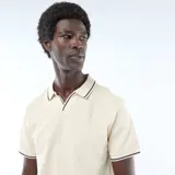 Remera polo de piqué de algodón color beige claro, de manga corta, con cuello y bordes de mangas en ribete negro y blanco.