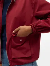 Campera parka corta de color bordó, con capucha ajustable, cierre frontal completo y dos bolsillos delanteros con solapa. Presenta puños elásticos y un diseño funcional y versátil.