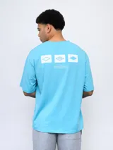 Remera de corte holgado color celeste, con cuello redondo diferenciado y logo de la marca estampado en el pecho. Presenta un diseño de manga corta y estilo deportivo.