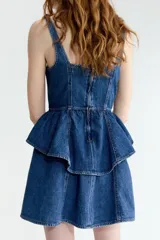 Vestido corto de denim azul con tirantes anchos, escote cuadrado, cuerpo entallado con costuras visibles y falda acampanada con doble volado en la cintura.