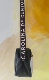 Bandolera Kaira de la línea Ottenta de Carolina de Cunto, color negro con bolsillo frontal dorado texturizado de efecto reptil y arte pintado a mano. Cuenta con correa regulable negra con el logo de la marca en blanco.