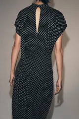 Vestido midi de viscosa con estampado de lunares blancos sobre fondo negro. Presenta cuello redondo con detalle de lazada, manga corta y pliegues en la cintura con bajo recto.