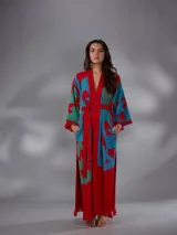 Kimono largo de algodón texturado con estampado vegetal en tonos rojo, azul y verde. Cuenta con mangas amplias, cinto independiente para ajustar a la cintura, bolsillos laterales y aberturas laterales en el dobladillo con detalles de flecos.