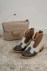 Botinetas estilo western de caña baja, confeccionadas en una combinación de cuero liso y gamuza en tonos marrón oscuro, marrón medio y crema. Presentan cierre lateral, taco bajo cuadrado y diseño con recortes característicos del estilo cowboy.