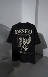 Remera de manga corta y cuello redondo con calce oversize. Presenta una estampa frontal en color crema con diseño artístico de un ángel y una rosa, acompañada de frases en español. Confeccionada en algodón premium.