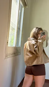 Campera corta de ecocuero color beige, con diseño de solapas y cierre frontal con botones a presión metálicos.