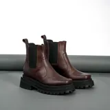 Bota tipo Chelsea de cuero vacuno color marrón, con paneles laterales elásticos, punta cuadrada y suela track de goma negra con plataforma.