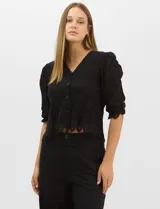 Blusa de algodón semitransparente con diseño floral bordado a tono. Presenta escote en V, cierre frontal con botones y mangas al codo ligeramente abullonadas. Incluye detalles de encaje calado estilo macramé en los puños y en el ruedo con terminaciones en ondas.