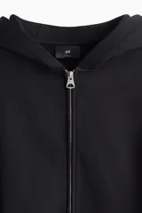 Campera con capucha de felpa pesada, con cierre frontal, bolsillos laterales y puños y bajo acanalados. Presenta un corte holgado y diseño minimalista.