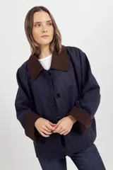 Chaqueta de corte amplio color azul marino, con cuello y puños vueltos en contraste color marrón. Presenta cierre frontal con botones oscuros y diseño de hombros caídos.