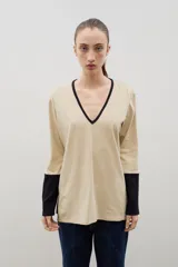 Remera de algodón con escote en V, manga larga y diseño bicolor. Presenta cuerpo en color beige con detalles en negro en el escote, los puños y los tajos laterales.