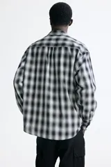 Camisa de corte relajado, confeccionada en mezcla de algodón suave con diseño a cuadros difuminados en tonos negro y blanco. Cuenta con cuello inglés, cierre frontal de botones, bolsillo en el pecho y mangas largas con puños abotonados.